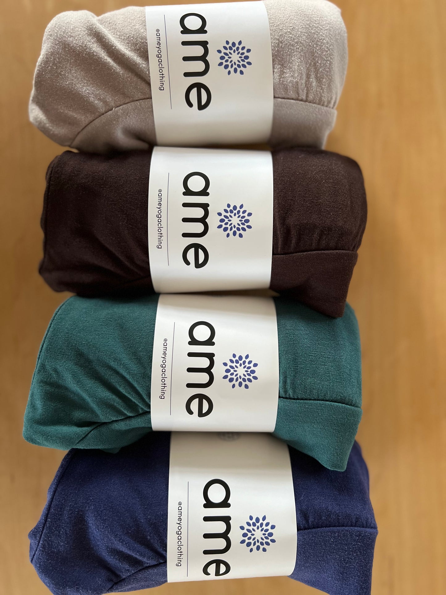 Four pairs of shorts in gray, brown, green, and blue with 'ame' branding on a wooden surface.