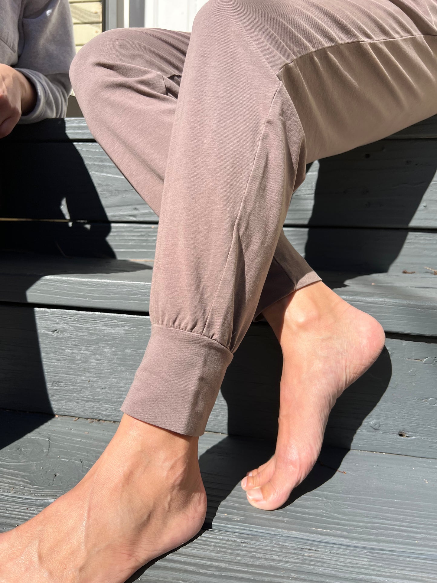 Person wearing a beige pant sitting on a wooden deck.