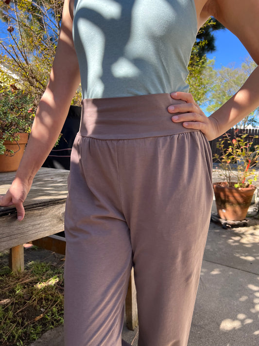 Person wearing light gray pants and a light blue shirt standing outdoors with trees and a clear sky in the background.