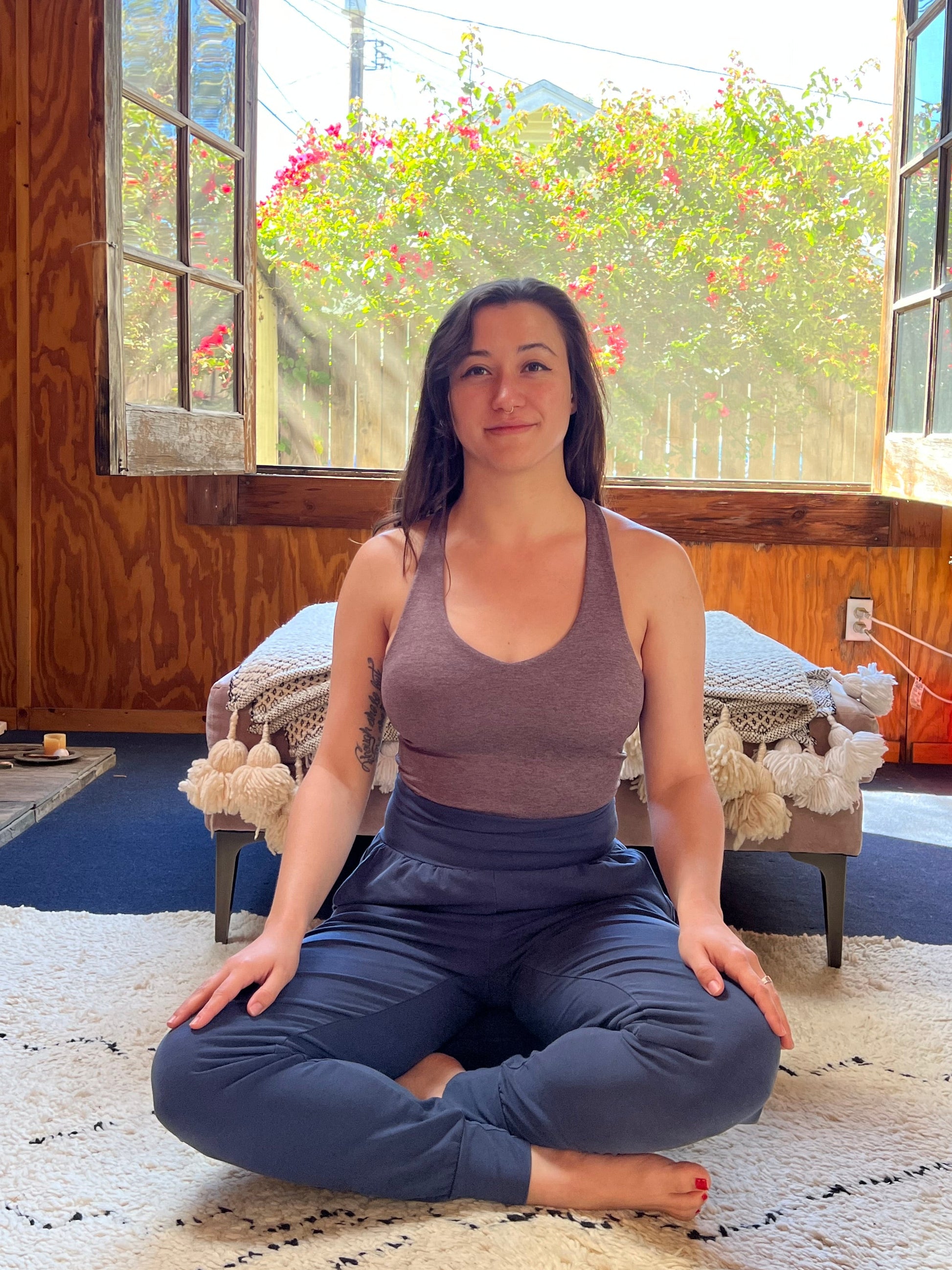 Woman in a yoga pose on a rug with a window and outdoor view in the background